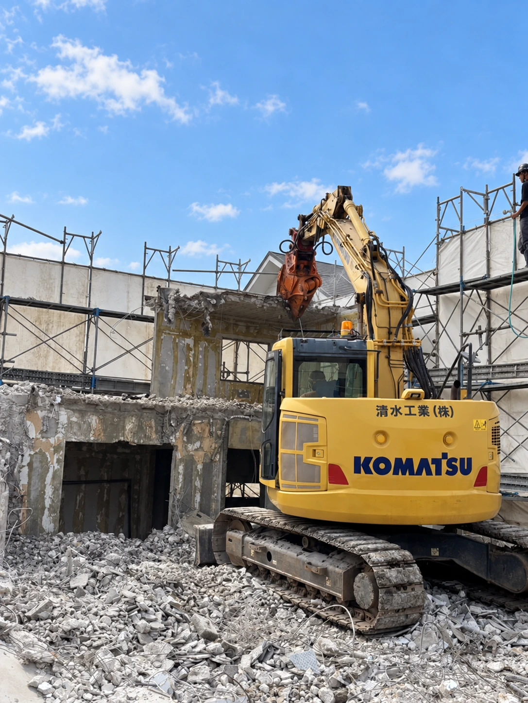 清水工業の社名が入った黄色い重機が建物を解体する現場
